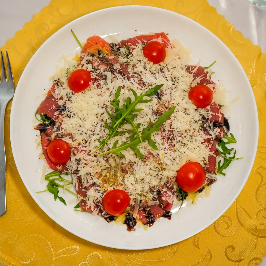 Goveji carpaccio s češnjevimi paradižniki, parmezanom in rukolo.